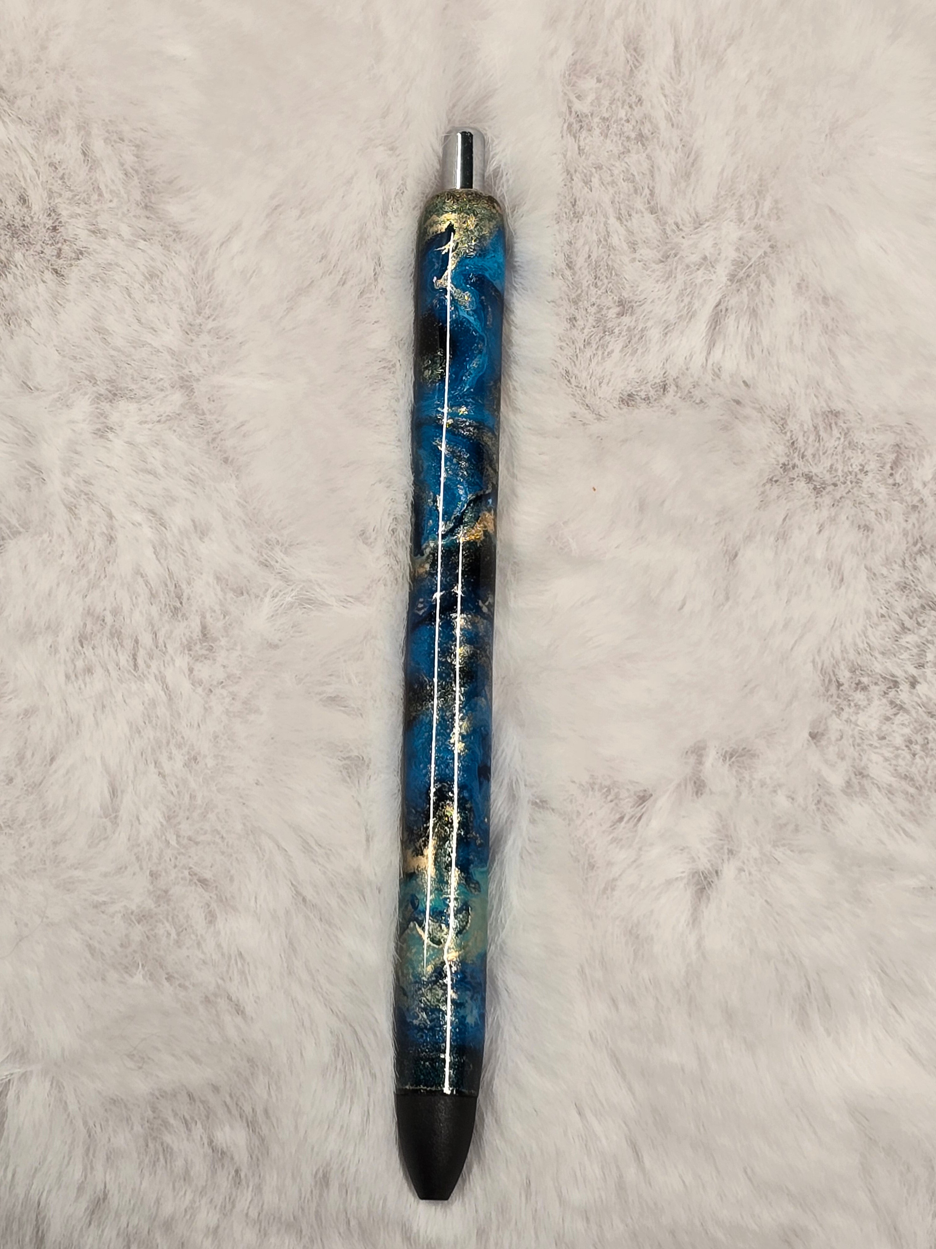 Pen with blue and gold marbled design on a textured black surface.