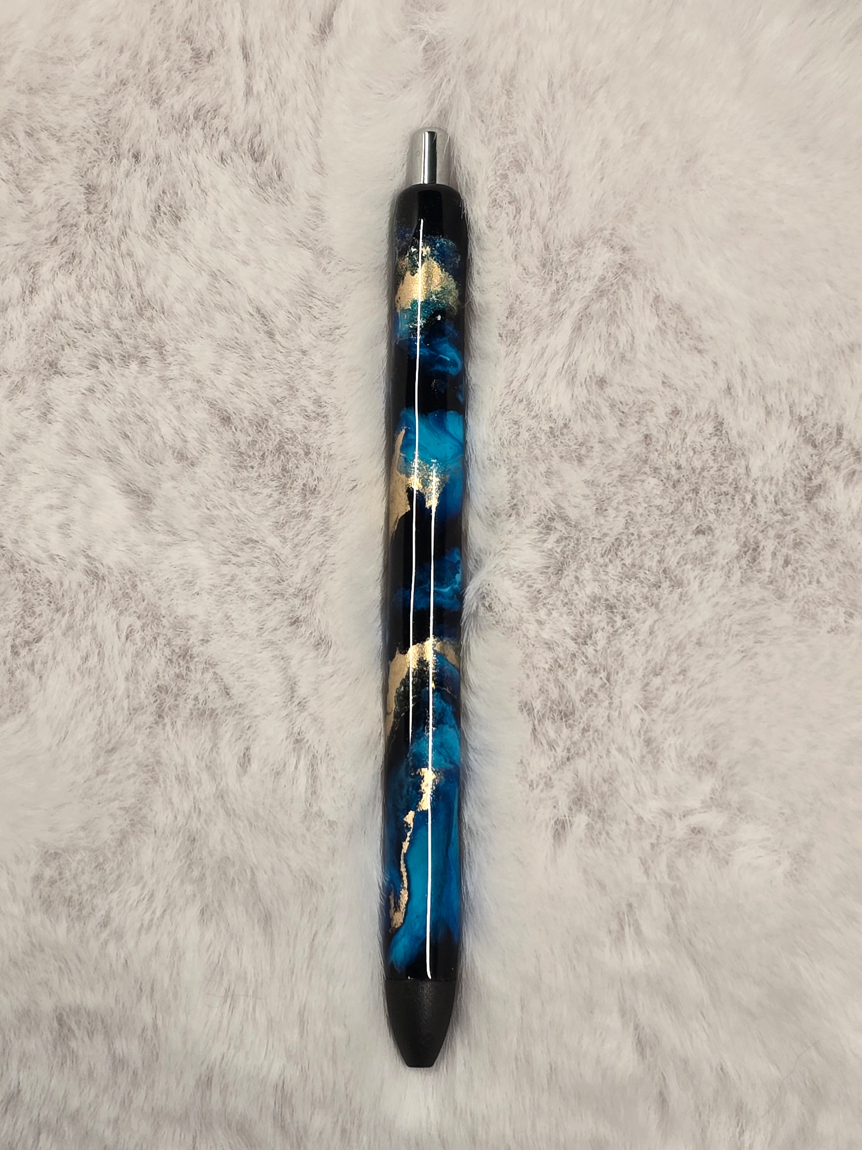 Decorative pen with blue and gold design on a black textured surface.